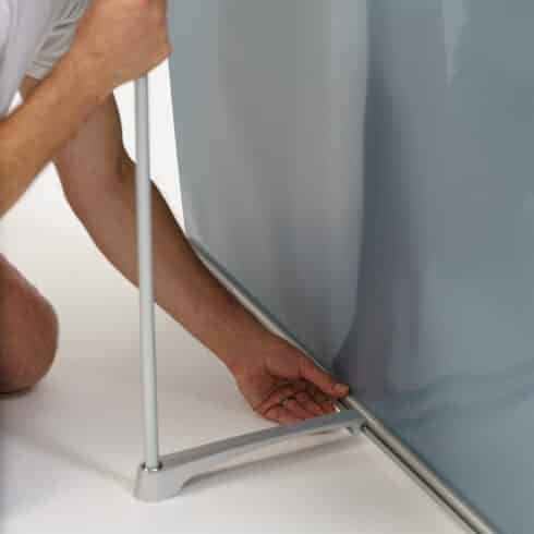 A person cliping the pole into the back of a tension wall banner stand
